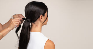 Stylist installing a ponytail hair extension on a woman with dark hair.